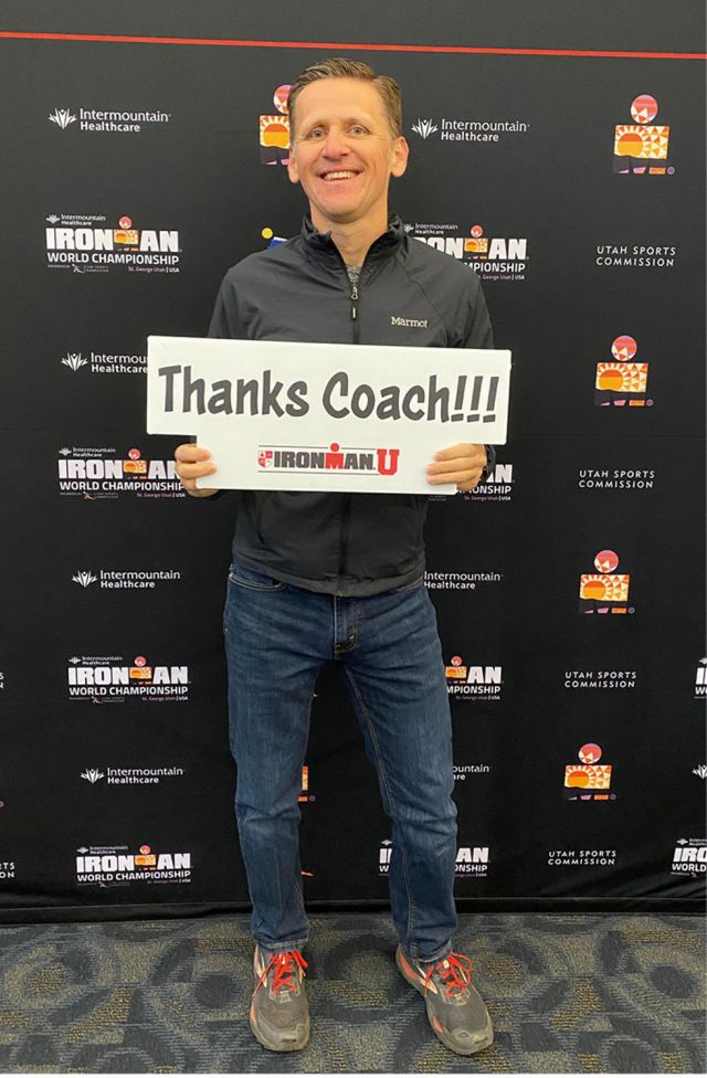 Athlet mit Marmot-Jacke hält Schild 'Thanks Coach!!!' vor Ironman World Championship Sponsorenwand