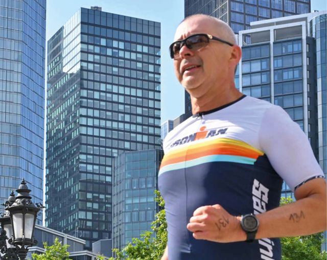 Albrecht Trölsch in Ironman-Trikot joggt vor Hochhauskulisse in einer Großstadt mit sonnigem Himmel
